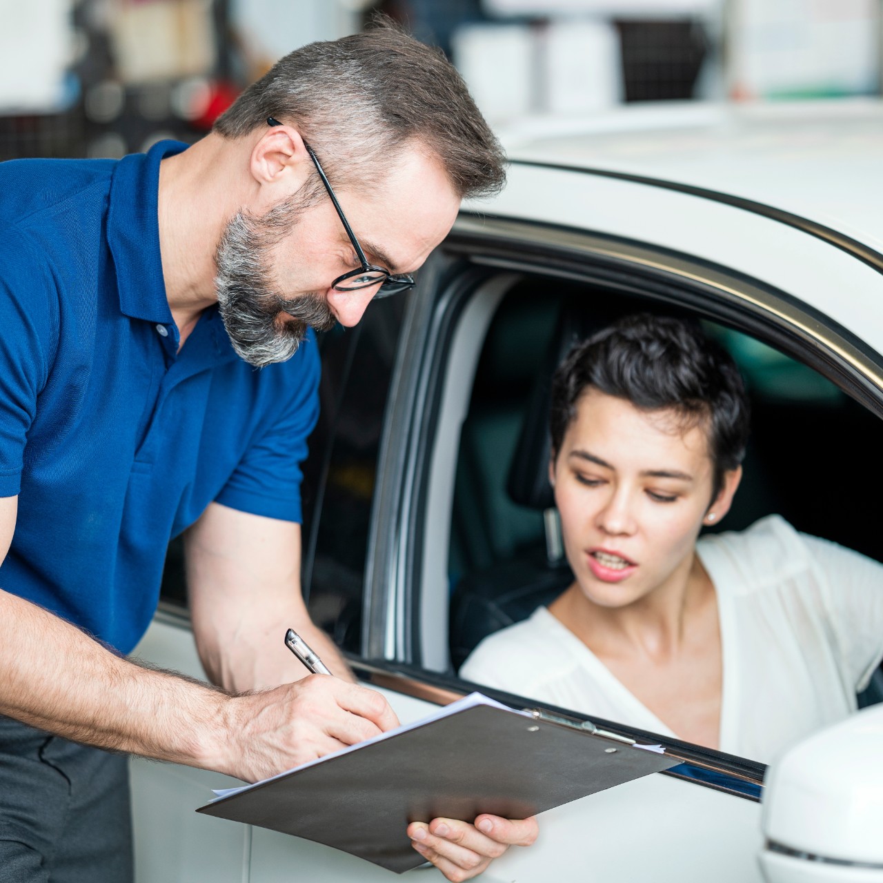 Caucasian auto mechanic with female client looking at car checklist with bill at Auto Repair Center. Female client sitting in car. Customer Service, Quality of Service.